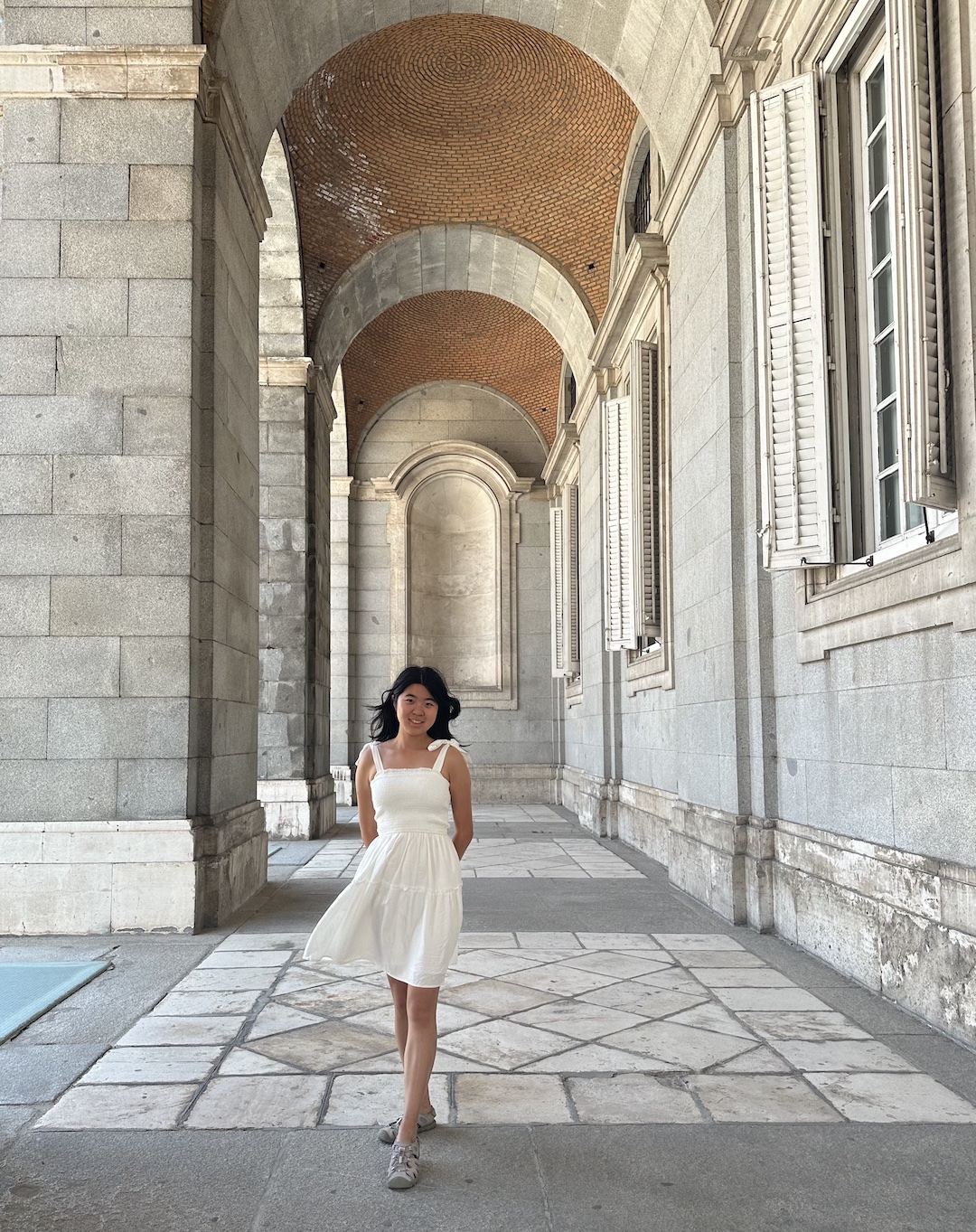 a girl stands in a white dress under a stone arch